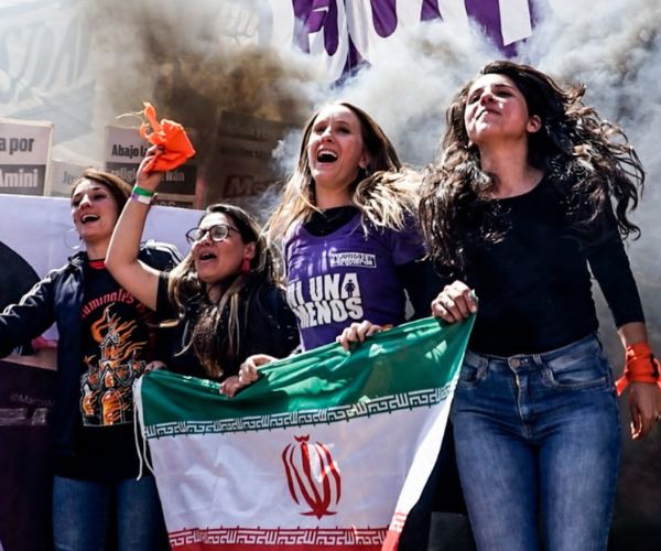 Luciana Echevarría saltando junto a Celeste Fierro en una marcha con bandera de Irán en la mano
