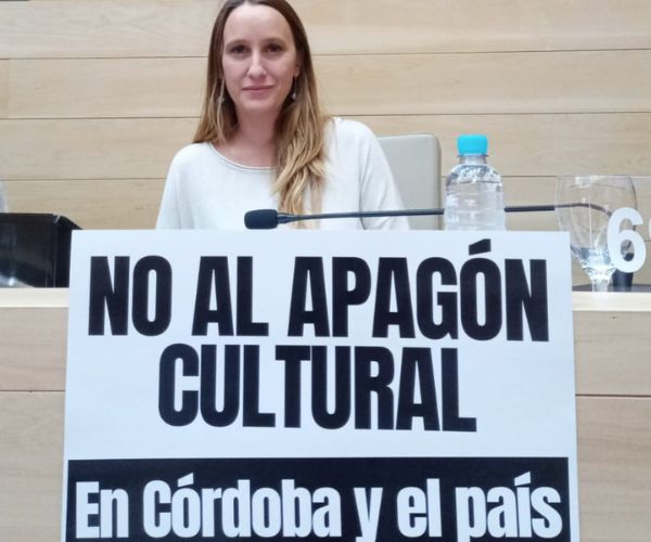 Legisladora Luciana Echevarría sentada en la legislatura de Córdoba con cartel frente a ella que dice no al apagón cultural en Córdoba y el país